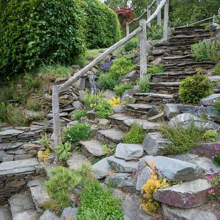 A mountain stream with waterfalls , rustic steps and rockery planting.
